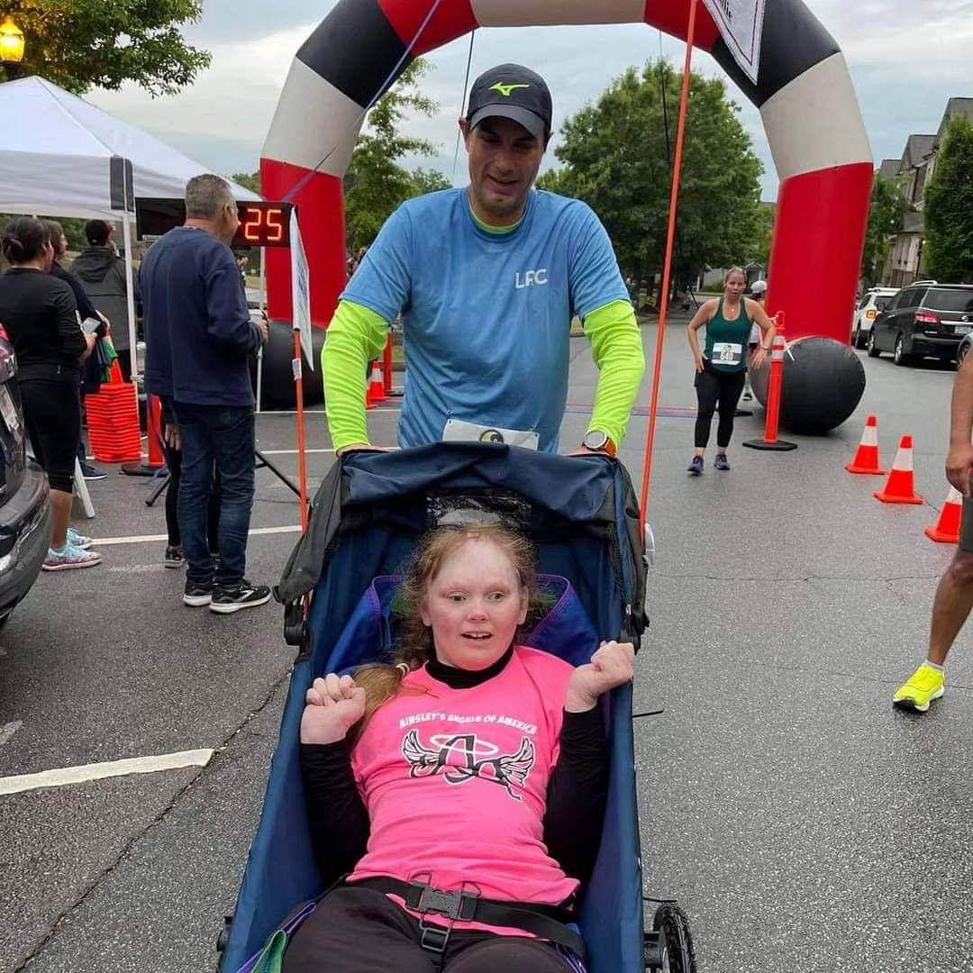 felipe niada pushing a rider chair at an ainsley’s angels 5k
