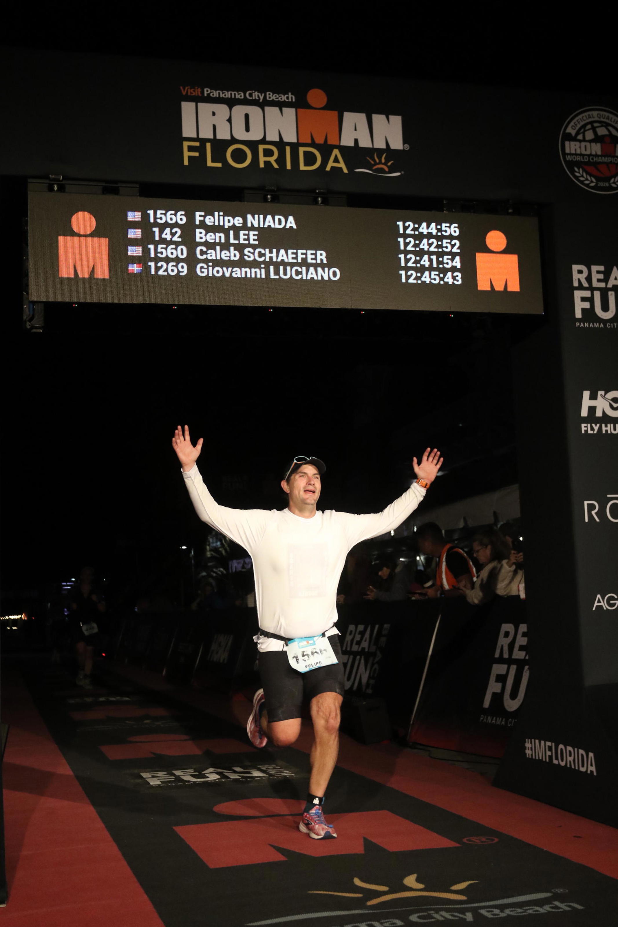 felipe niada crossing the ironman finish line at night with arms raised