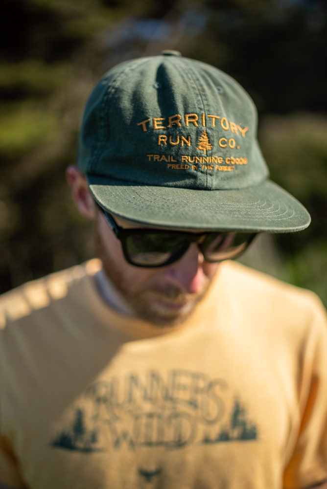 close-up of a green territory run co cap with gold embroidery reading trail running goods, freed by the forest