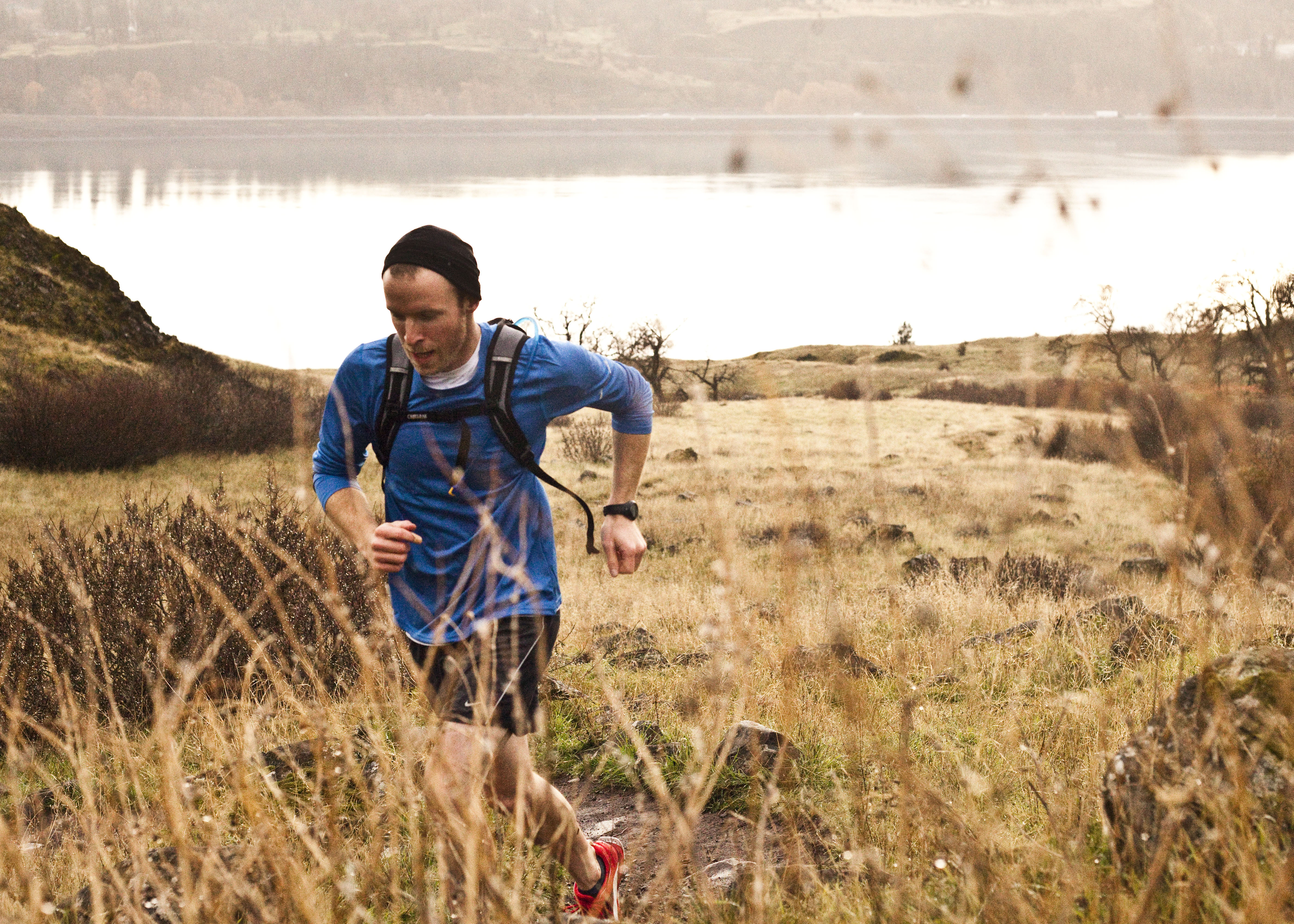 a runner moving through golden grass on an open trail near the water